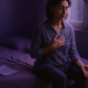 Mujer sentada junto a la ventana trabajando su sentimiento de culpa con la mano en el pecho