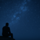 Hombre sentado a oscuras al borde de la cama al amanecer, una franja de luz cruza el suelo: noche oscura del alma