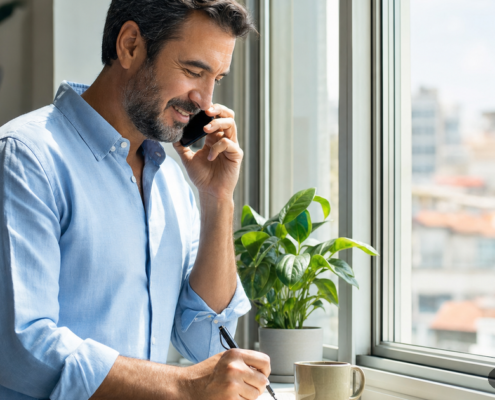 Hombre hablando por teléfono y tomando notas junto a una ventana: prácticas energéticas Valencia opiniones y dudas